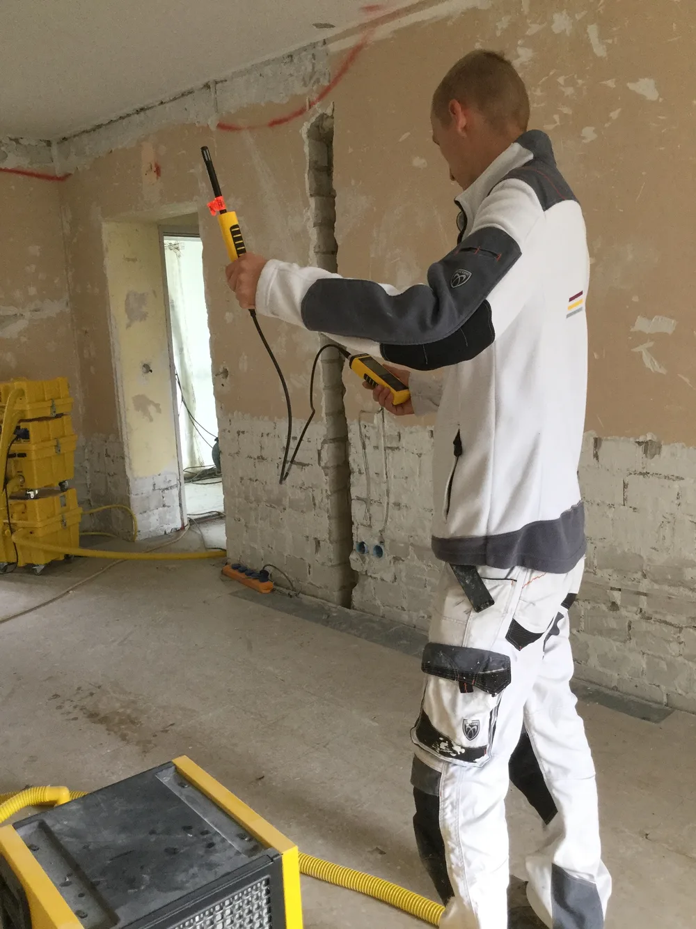Messung der Feuchtigkeit an einer zurückgebauten Wand, im Hintergrund ein Bautrockner.