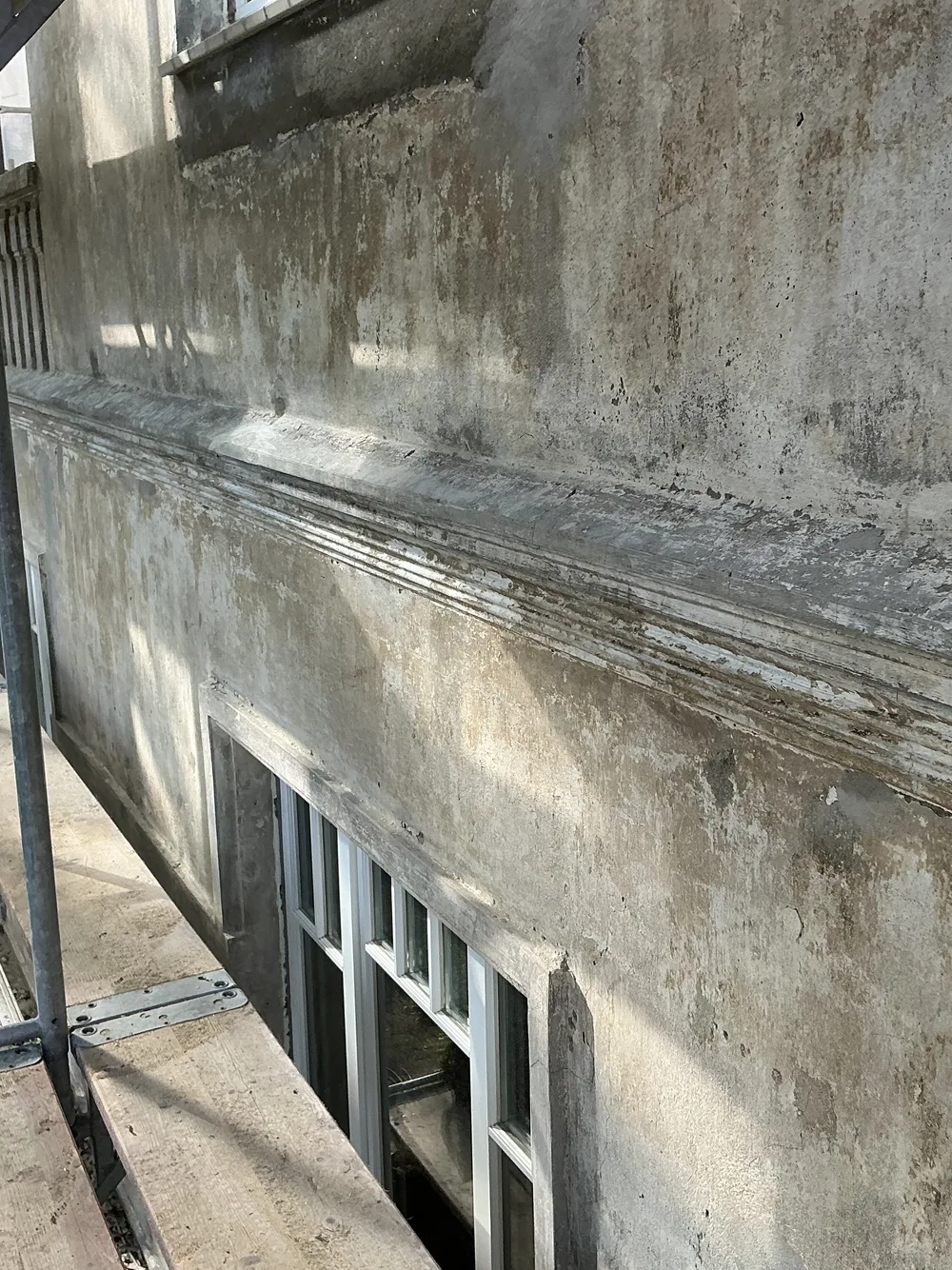 Verwitterte, dunkel verfärbte Altputz-Fassade mit Gesims, eingerüstet vor der Sanierung